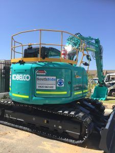 A green and yellow excavator is parked on the side of the road.