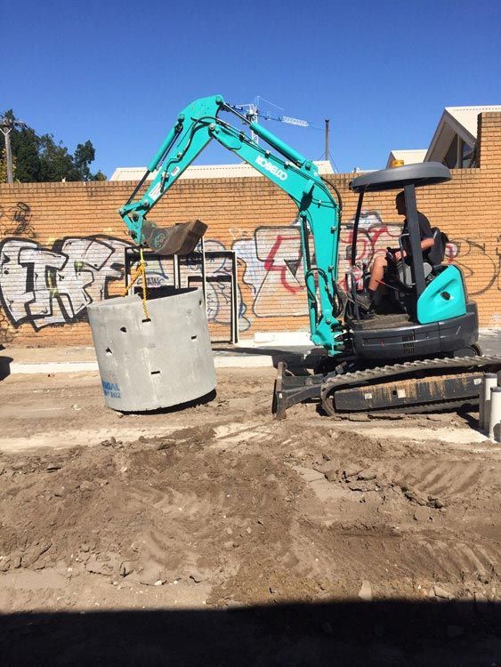 A large concrete pipe is being lifted by an excavator.
