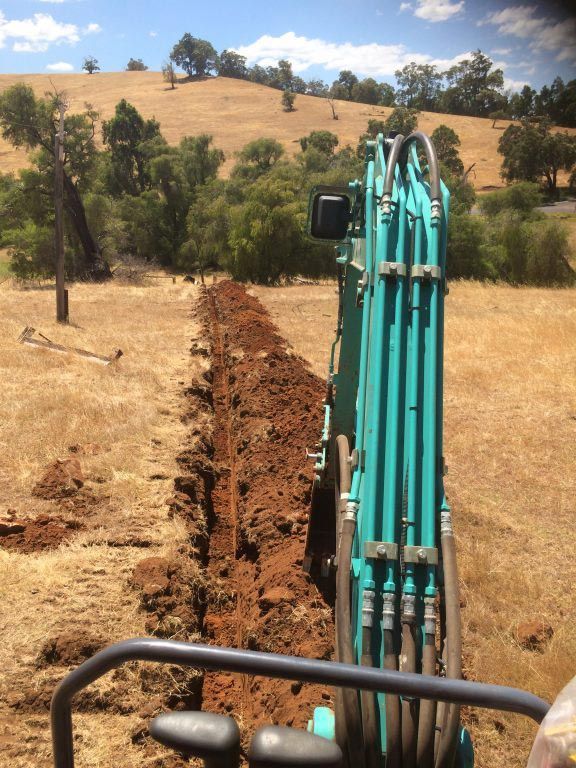 A blue excavator is digging a trench in a field