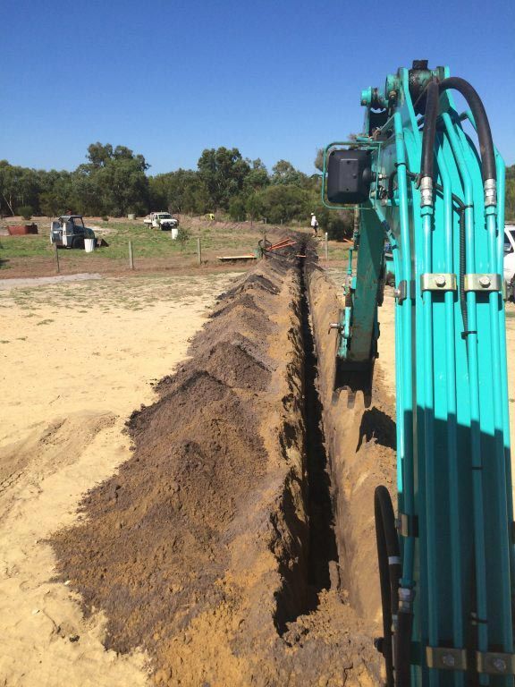 A blue excavator is digging a trench in the dirt
