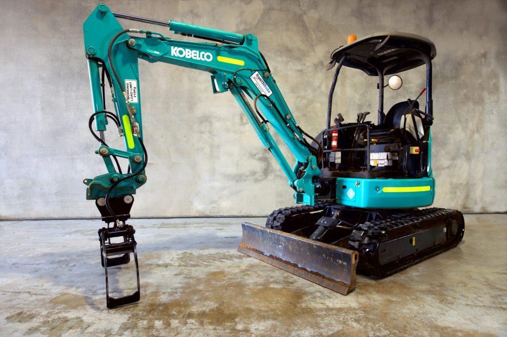 A kobelco excavator is sitting on a concrete floor.
