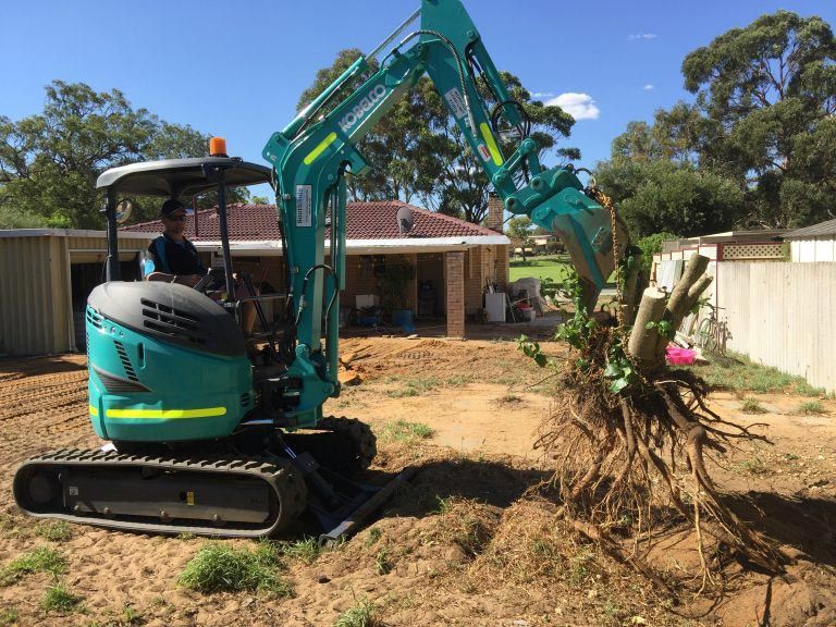 A man is driving a small excavator in a dirt field.