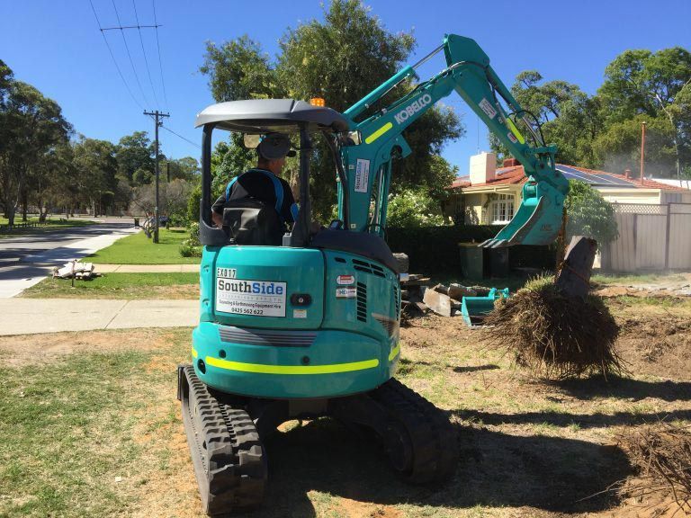 A man is driving a small excavator in a yard.