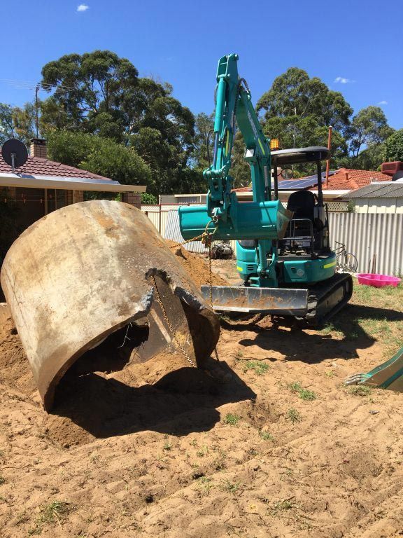 An excavator is digging a hole in the dirt in front of a house.