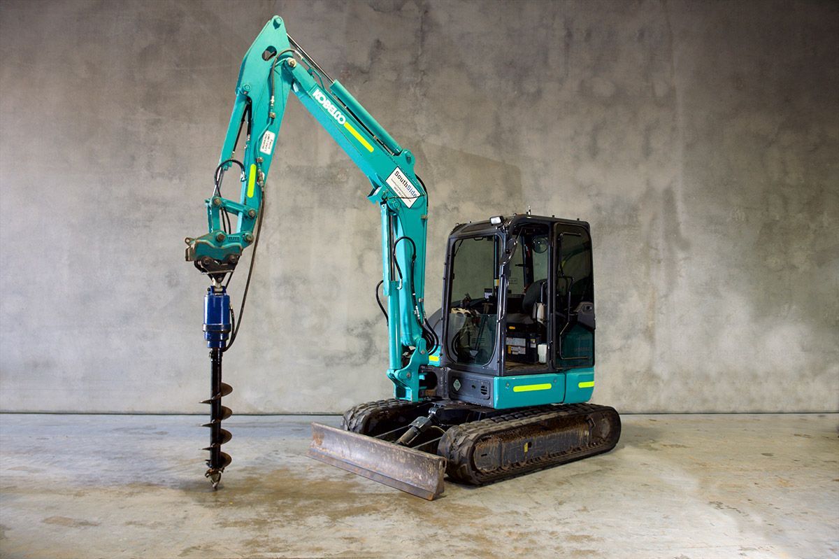 A blue excavator with a drill attached to it is sitting on a concrete floor.