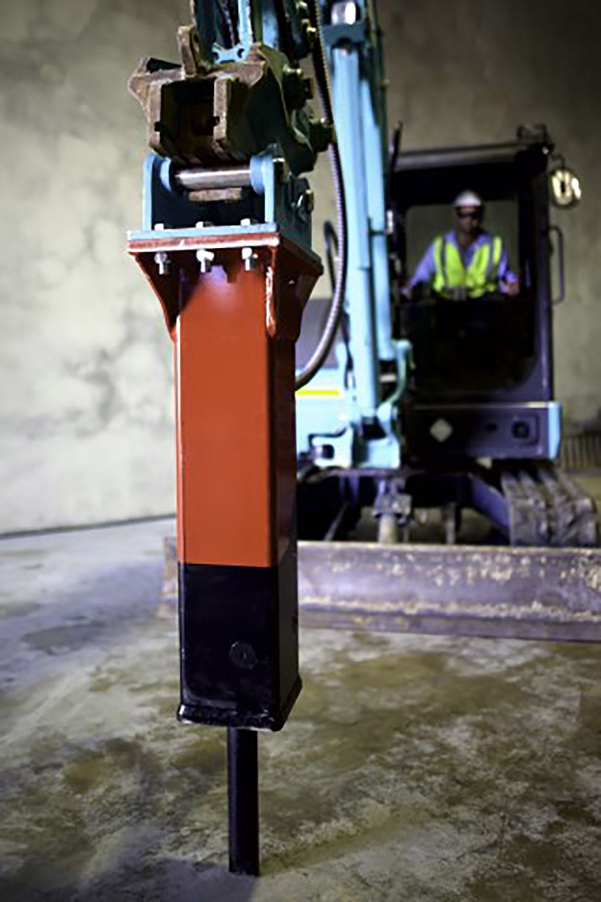 A man is driving an excavator with a hammer attached to it.