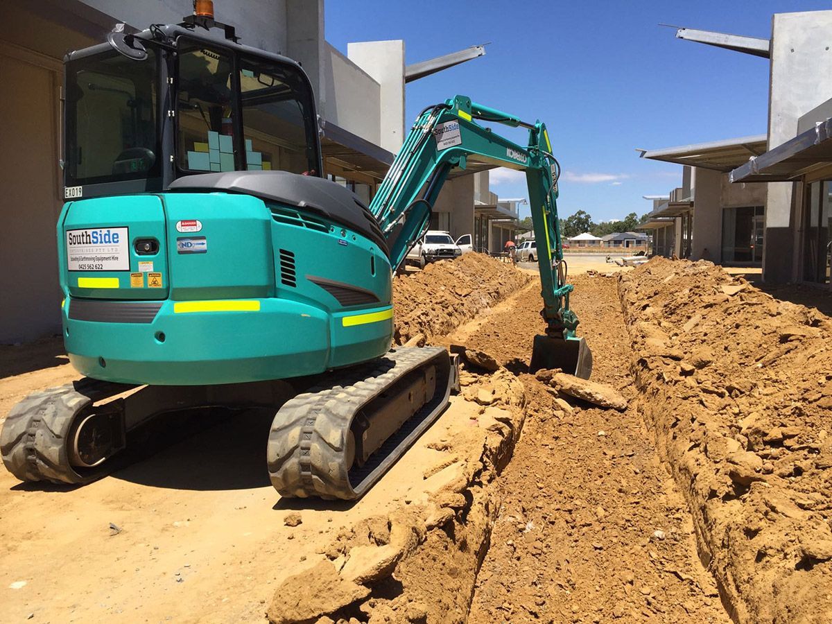 A small green excavator is digging a hole in the dirt.