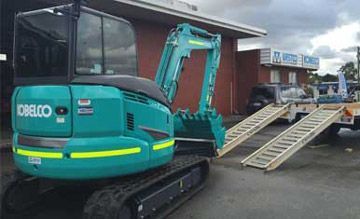 A small blue excavator is parked in front of a building.