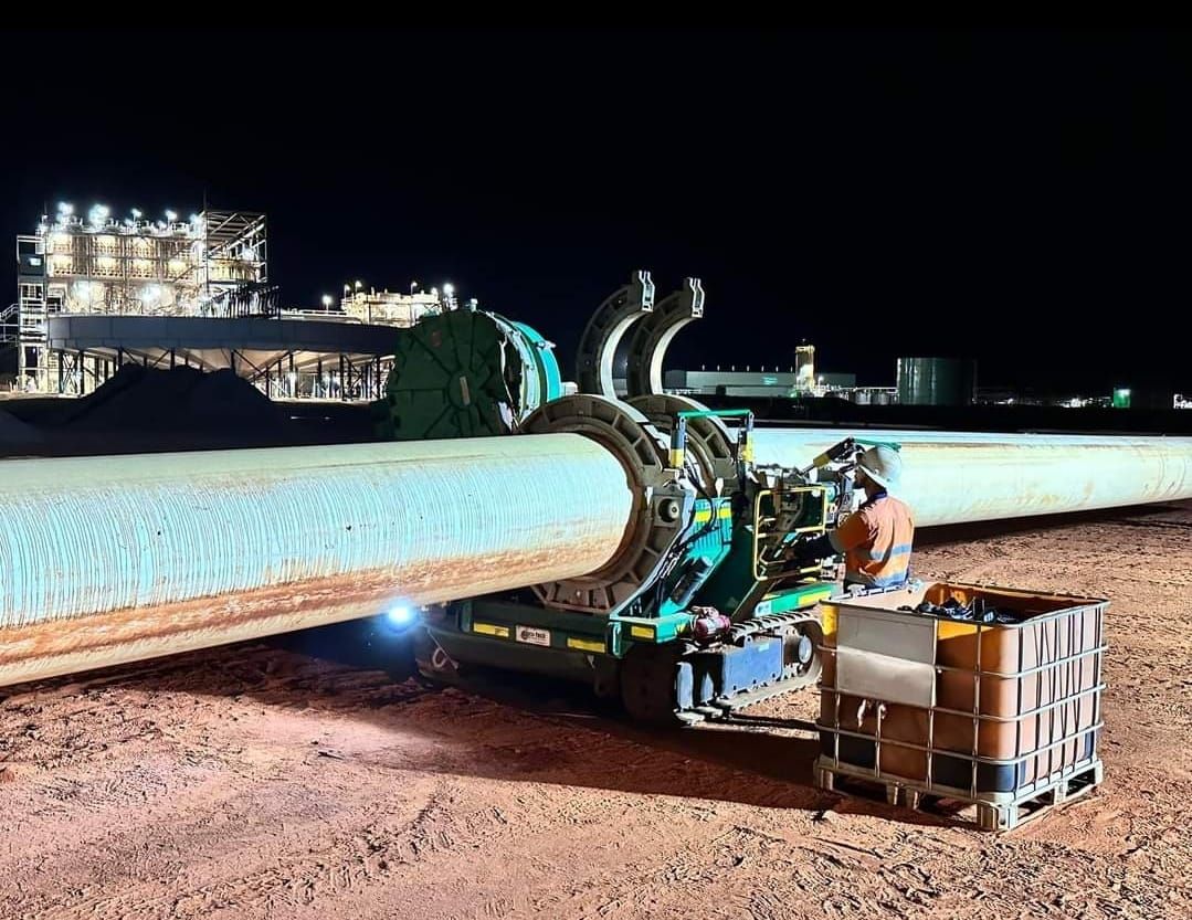 A man is working on a large pipe at night.