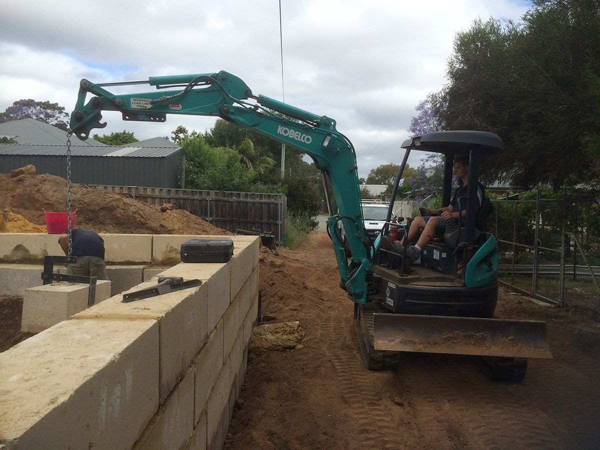 A man is driving a small green excavator on a dirt road.