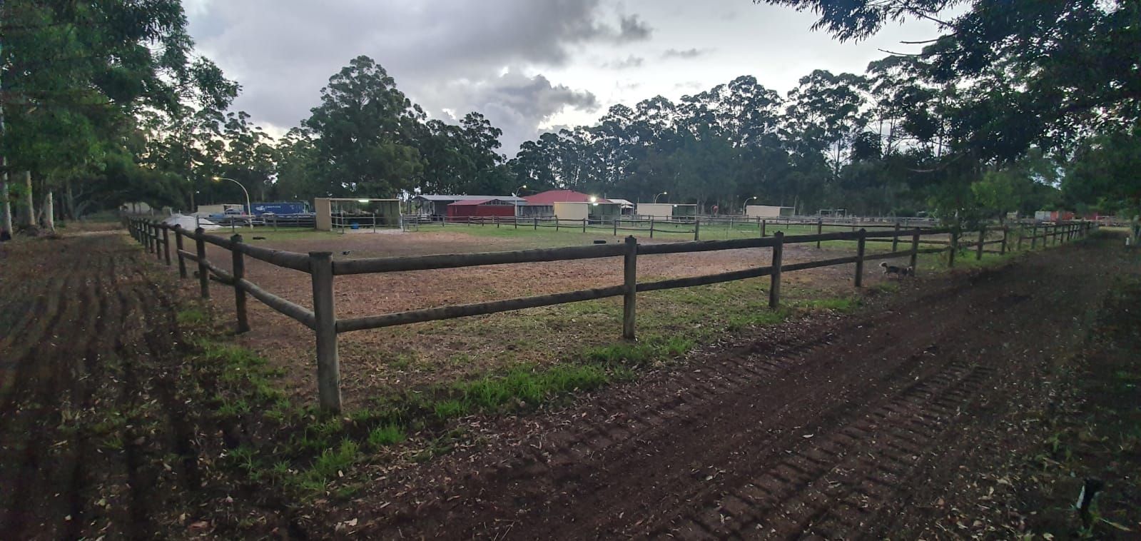 A wooden fence surrounds a dirt field with trees in the background