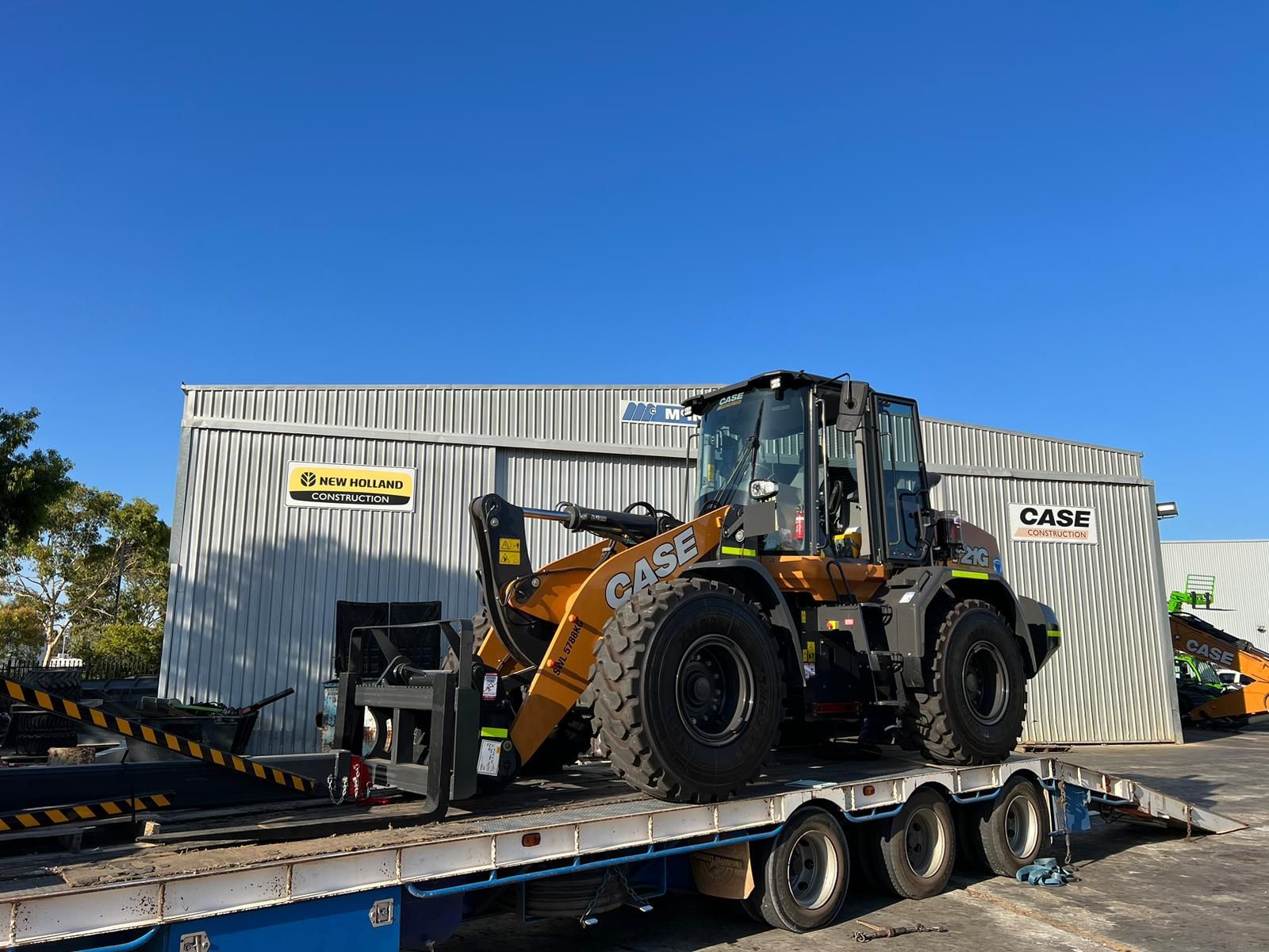 A bulldozer is sitting on top of a trailer in front of a building.