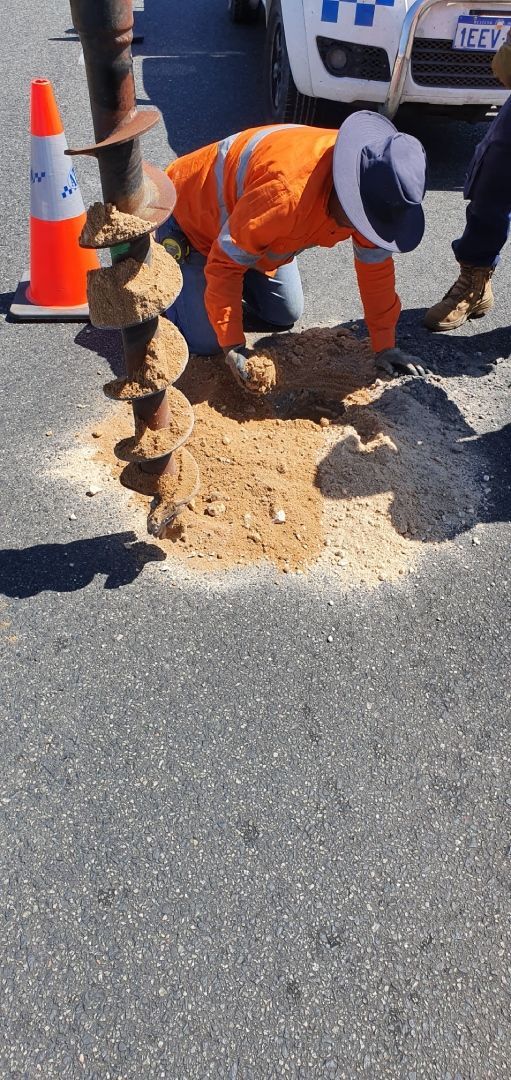 A man is digging a hole in the ground on the side of the road.