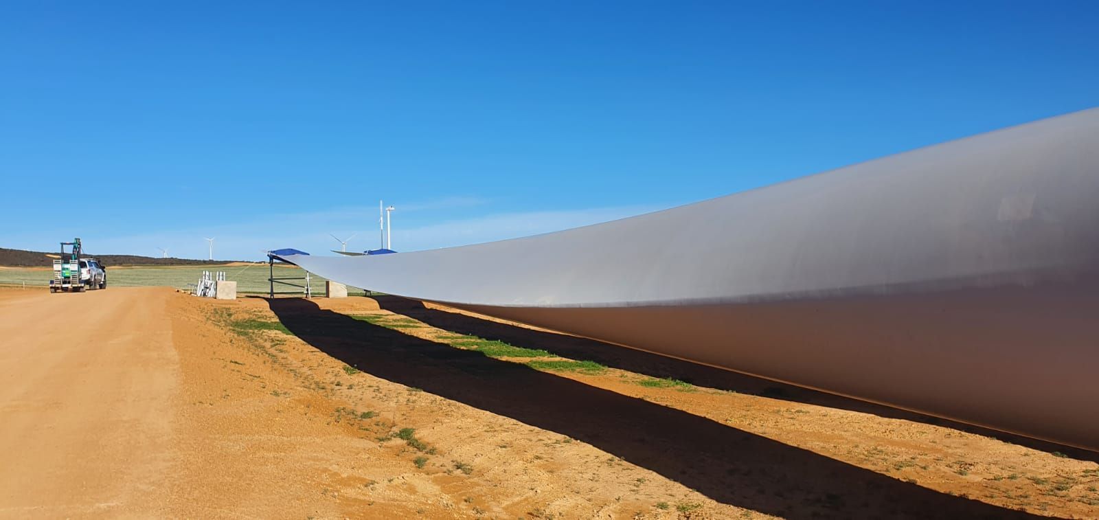 A wind turbine is sitting on the side of a dirt road.