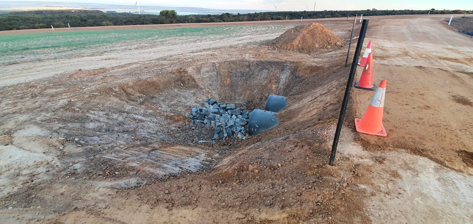 A muddy field with a fence and traffic cones in the foreground.