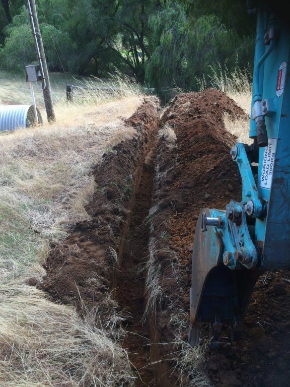 A blue tractor is digging a trench in the dirt.