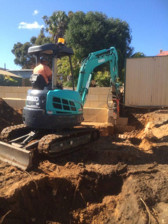 A man is driving an excavator in a dirt field.