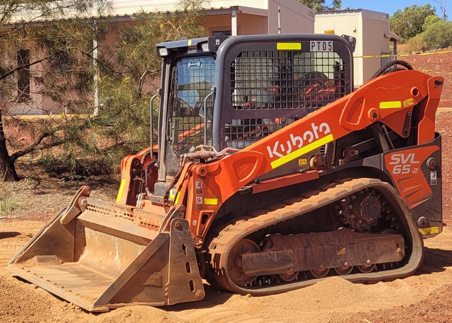 A kubota skid steer is parked in the dirt in front of a building.