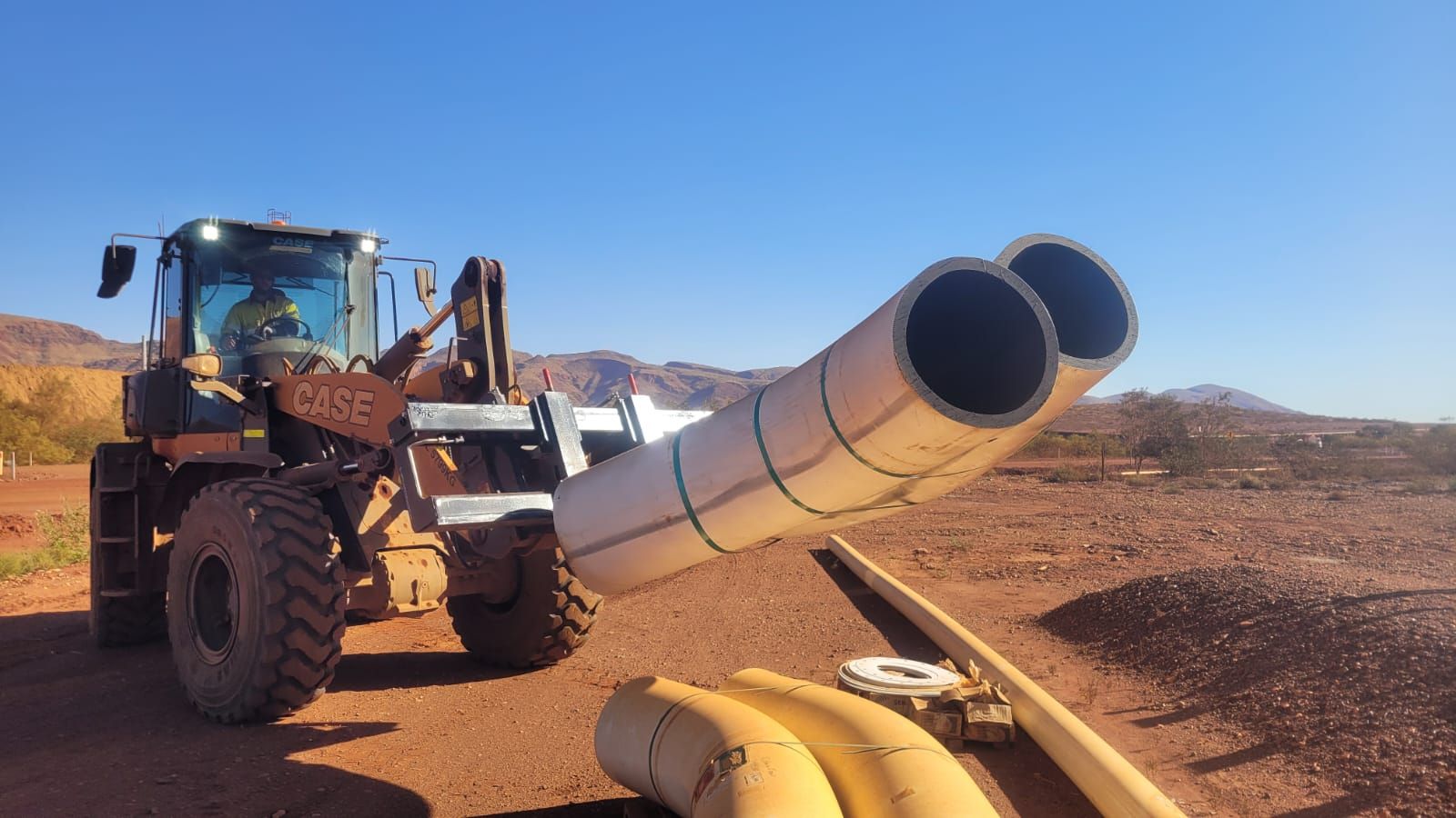 A tractor is carrying a bunch of pipes in the dirt.
