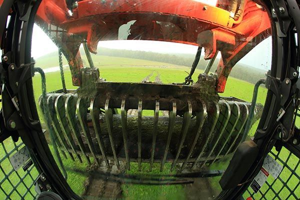 A close up of a machine in a field with a fence in the background.