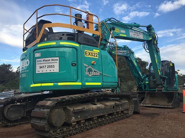 A green excavator is parked next to a bulldozer on a dirt road.