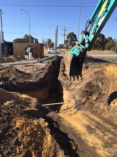 A green excavator is digging a hole in the ground.