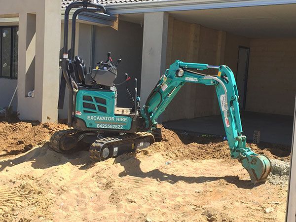 A small excavator is sitting in the dirt in front of a house.