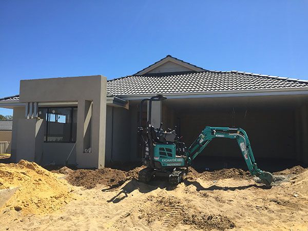 A small green excavator is sitting in front of a house under construction.