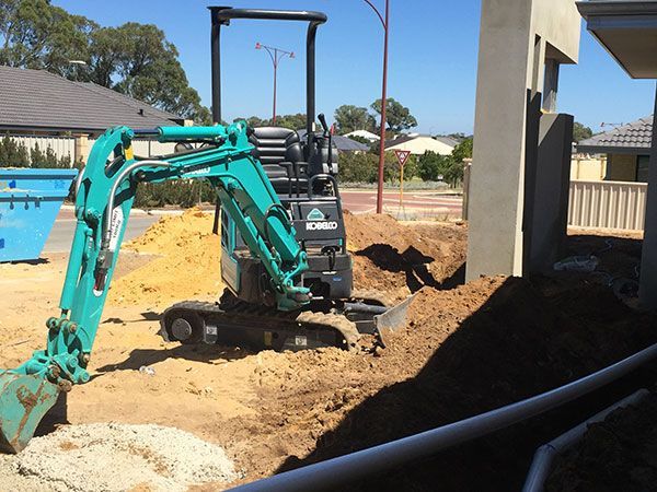 A small green excavator is digging a hole in the dirt