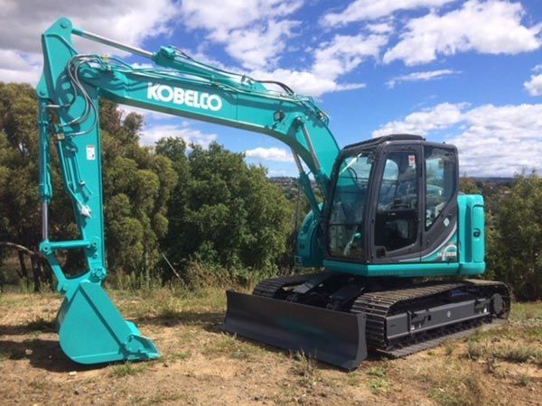 A kobelco excavator is parked in a grassy field.