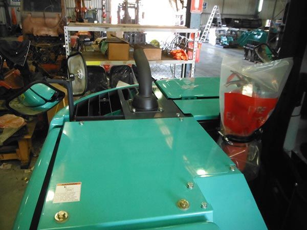 A blue tractor is sitting in a garage with a bag of red liquid in front of it