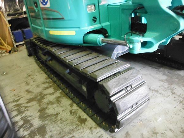 A green excavator is sitting on the ground in a garage