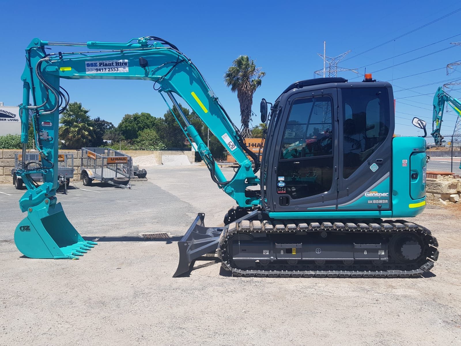 A small blue excavator is parked in a gravel lot.
