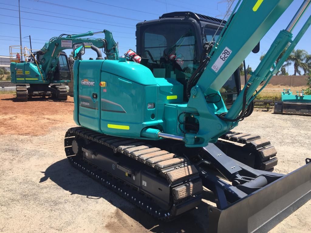 A blue excavator is parked in a dirt lot
