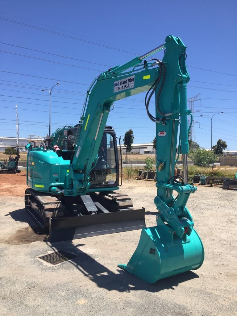 A green excavator is parked in a parking lot.