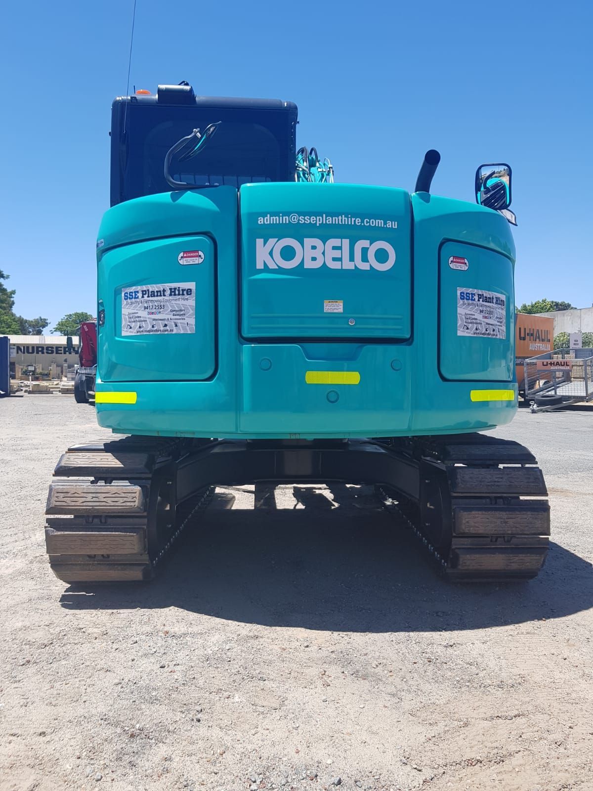A blue kobelco excavator is parked in a dirt lot.