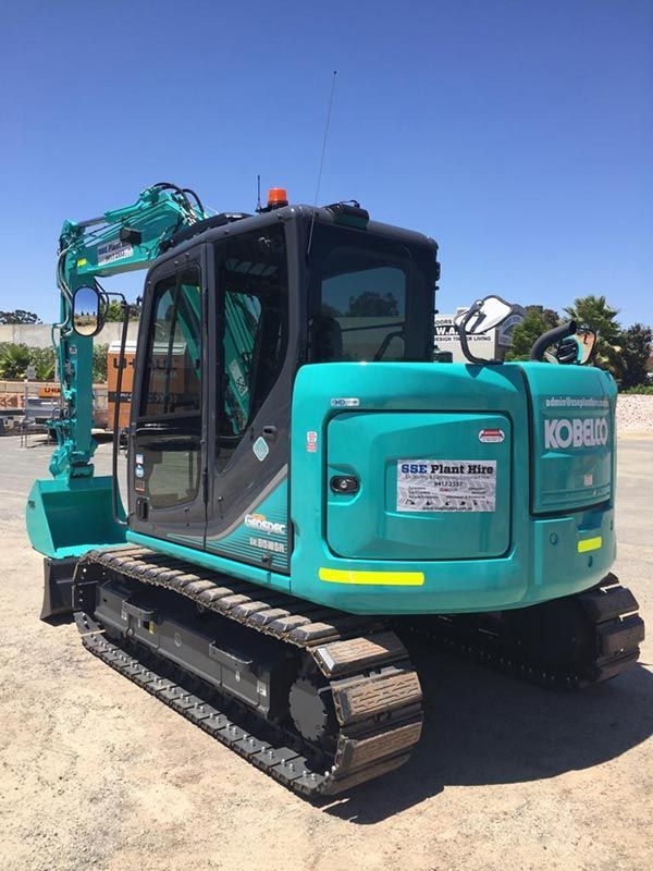 A blue and black excavator is parked in a parking lot.