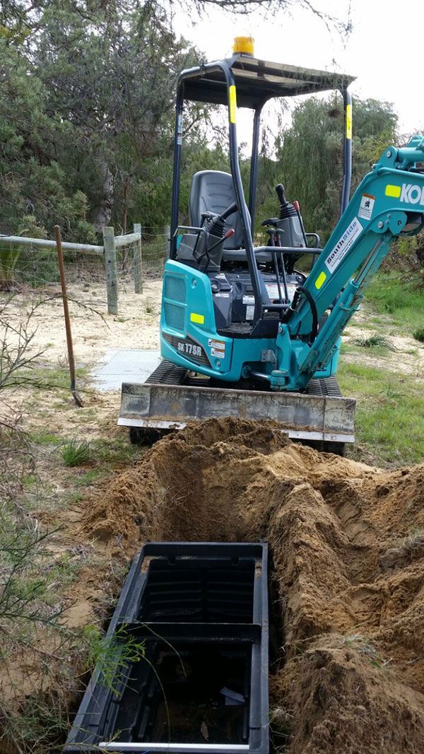 A small blue excavator is digging a hole in the ground.