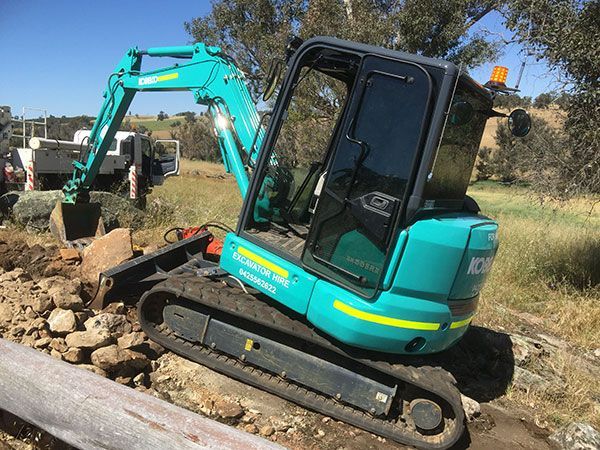 A small blue and green excavator is sitting on top of a pile of rocks.