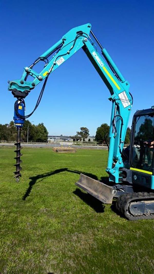 A blue excavator is digging a hole in the grass.