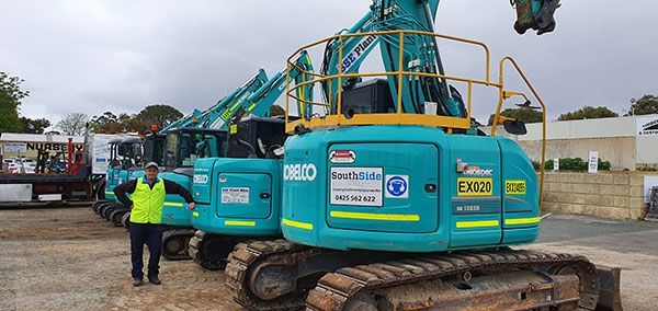 A man is standing in front of a row of construction vehicles.