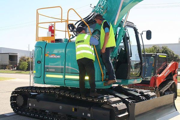Two men are standing on top of a blue excavator.