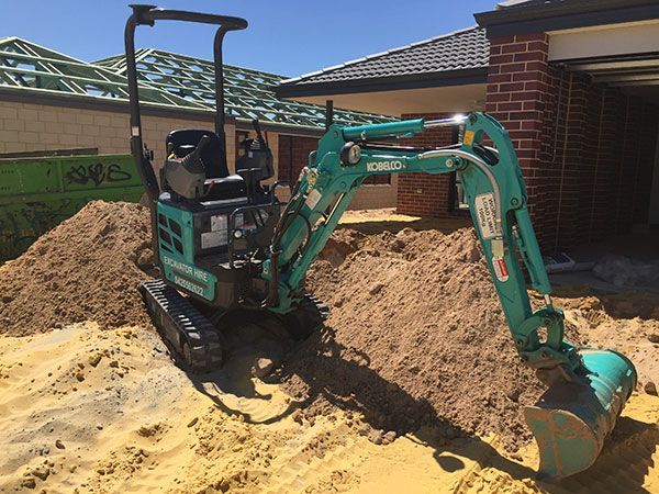 A small excavator is sitting in the dirt in front of a house.