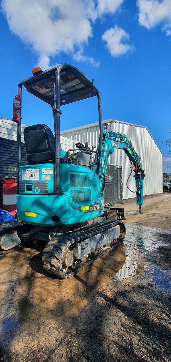 A small excavator is parked in front of a building on a dirt road.