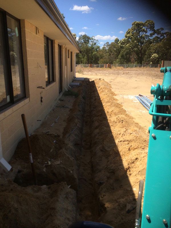 A green tractor is digging a hole in the dirt in front of a house