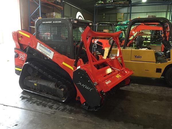 A red tractor is parked next to a yellow forklift in a garage.