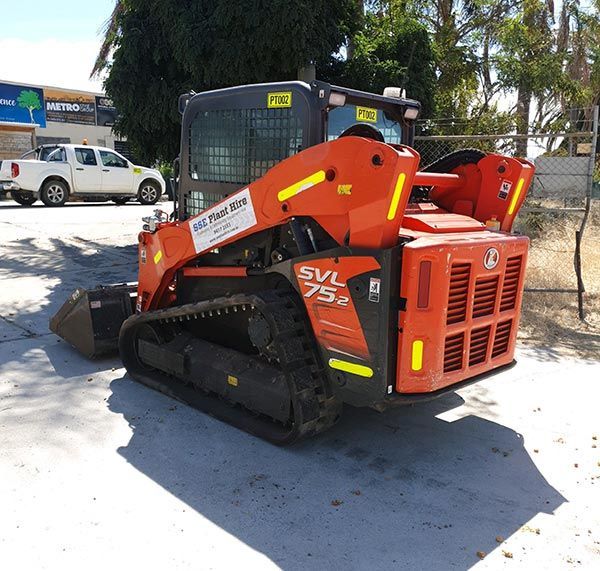 An orange and black skid steer is parked in a parking lot