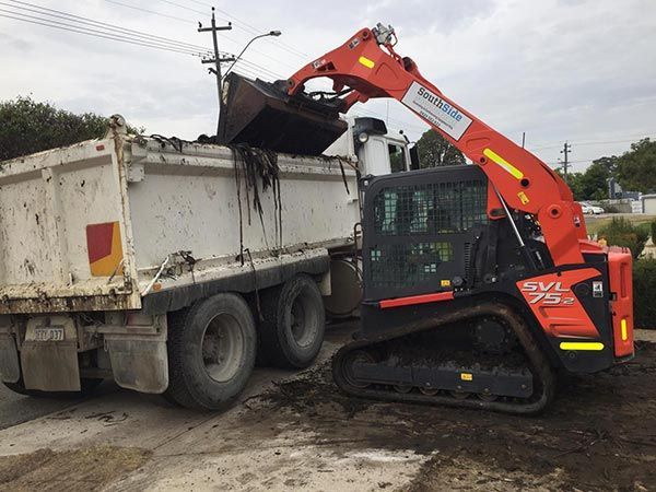 A bulldozer is loading dirt into a dump truck.