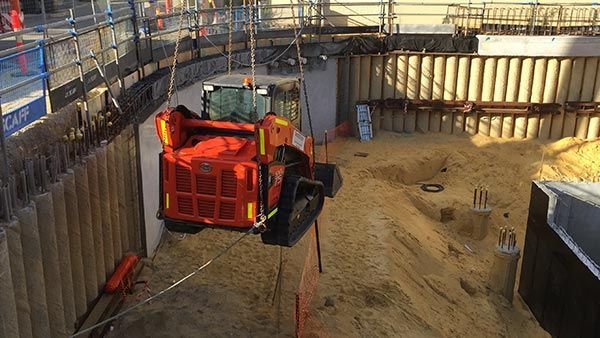 A bulldozer is being lifted by a crane in a construction site.