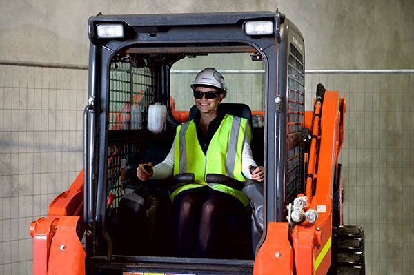 A woman is sitting in the driver 's seat of an orange tractor.